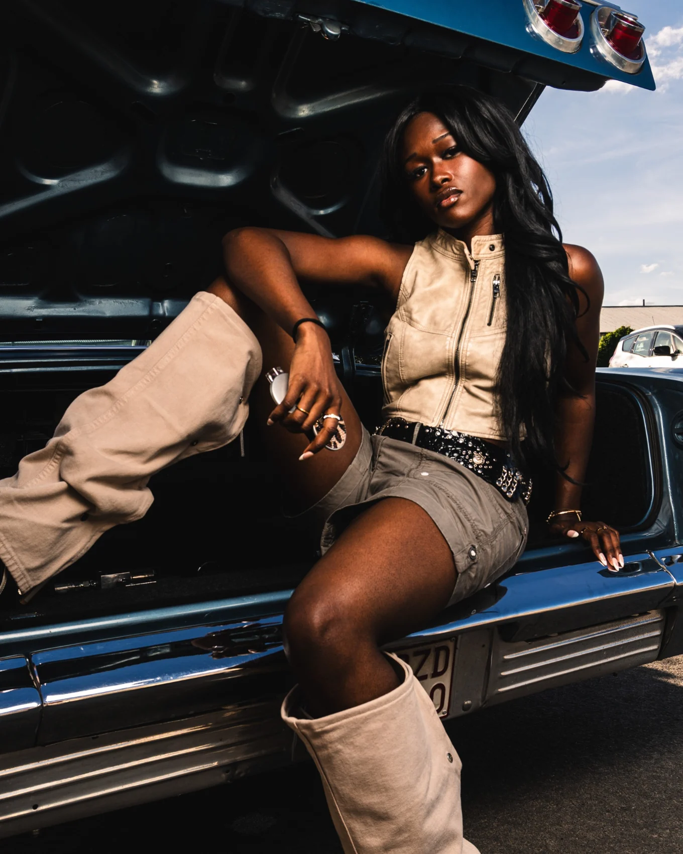 A neutral look with tall boots beside a vintage car.