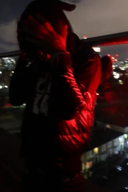 A red-lit portrait with raised hands and a black puffer vest.