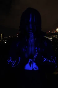 A blue-lit portrait with hands together against the night skyline.