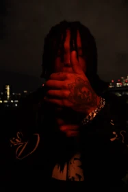 A close portrait with a tattooed hand and silver bracelet under red light.