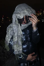 A patterned scarf draped over the head with a black puffer vest.
