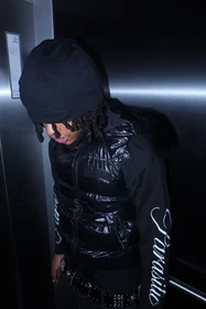 A black beanie and puffer vest against the brushed-metal elevator walls.