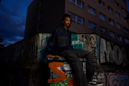 A seated outdoor portrait in the denim jacket with the full silhouette visible.
