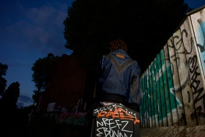 The rear silhouette of the denim jacket beside the graffiti wall.