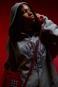 A grey hooded knit look with a red telephone against the red studio backdrop.