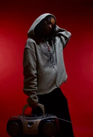 A grey hooded knit look with a boombox against the red studio backdrop.