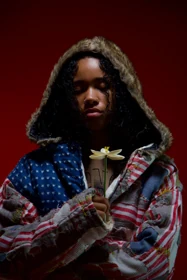 A close portrait in the patchwork jacket with a white flower.