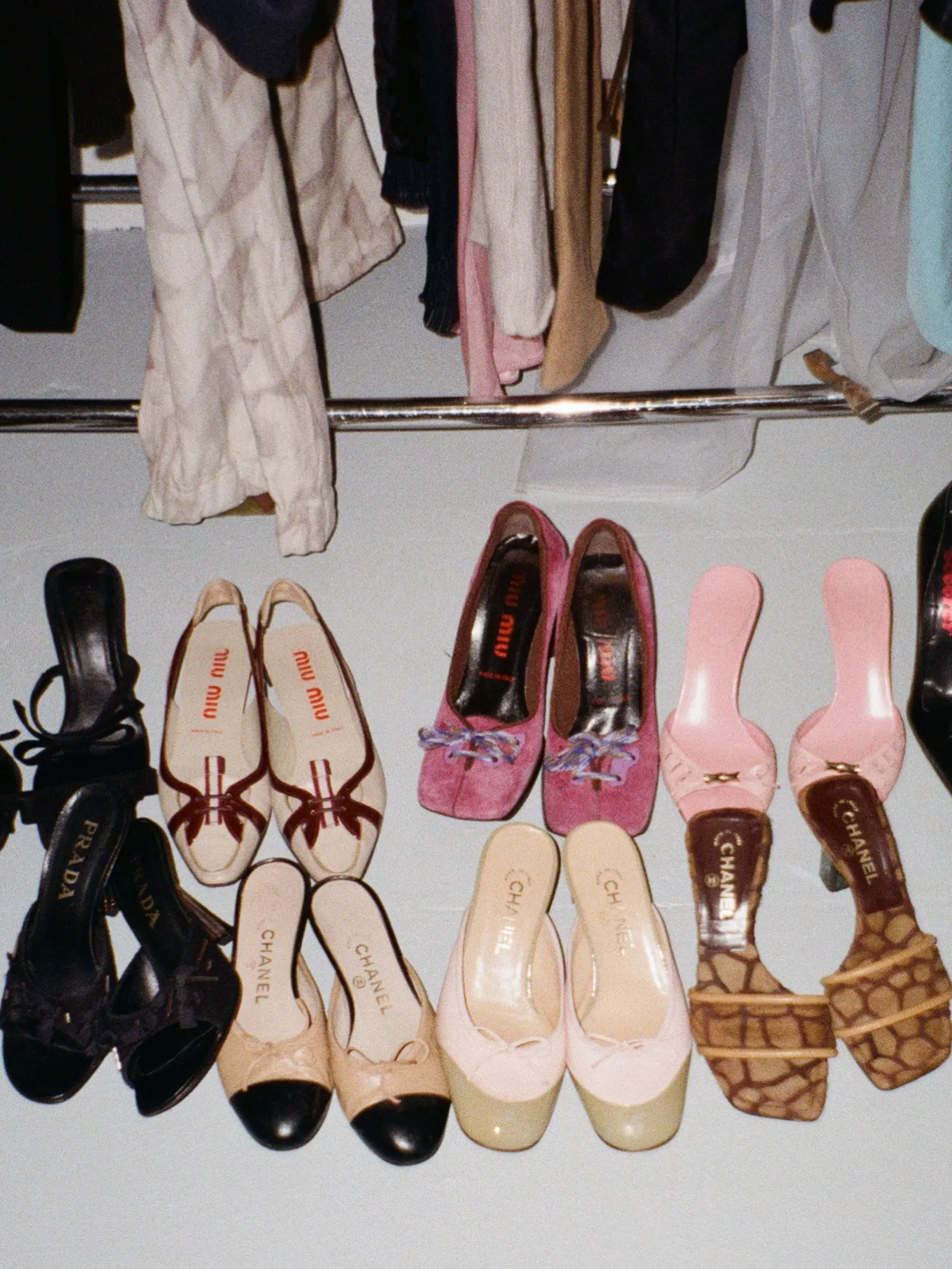 A selection of shoes in black, cream and pink beneath a clothing rail.